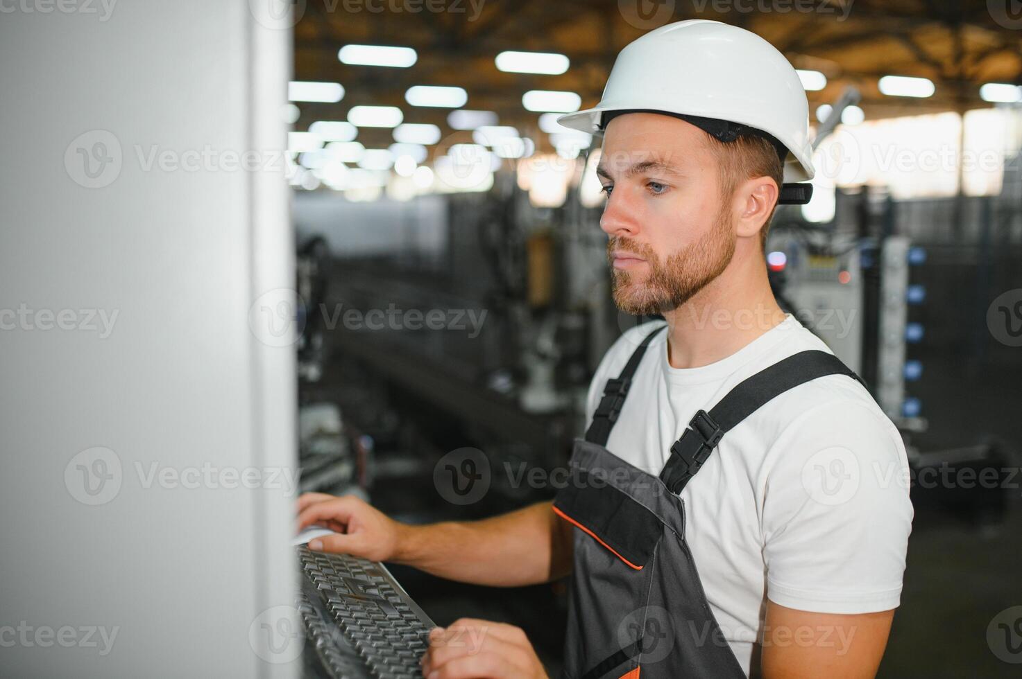 Factory male bearded worker is programming a CNC milling machine with copy space photo