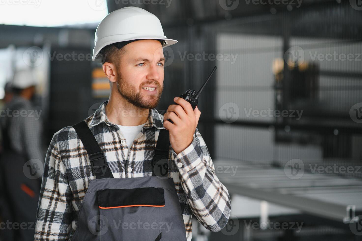 Smiling and happy employee. Portrait of industrial worker indoors in factory. Young technician with white hard hat photo