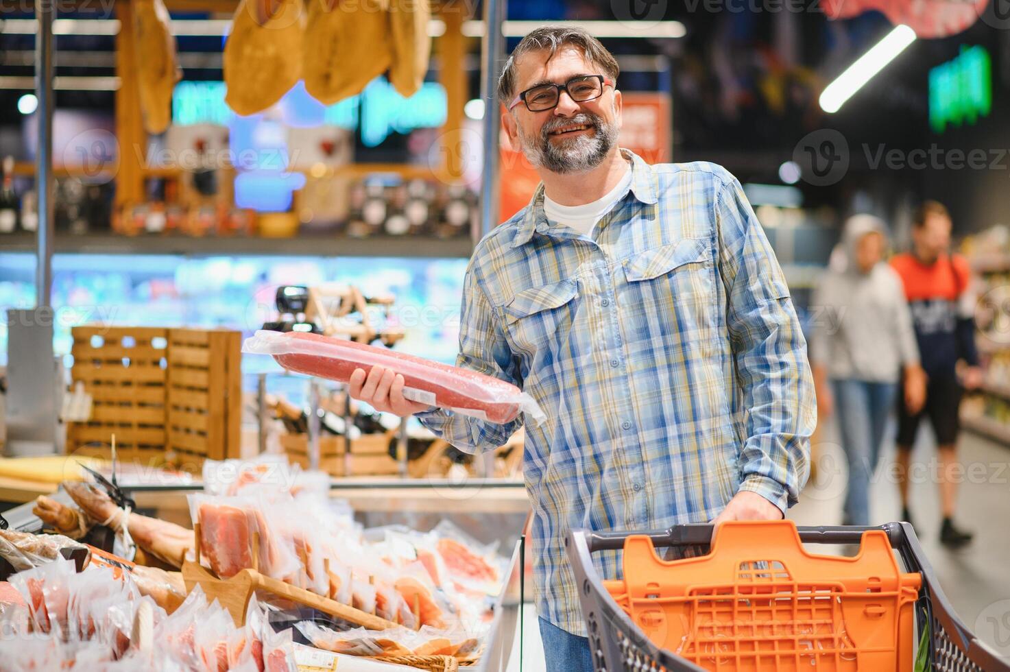 Elderly man buyer of meat department of grocery store, holding at meat sausage. Male pensioner customer orders meat snacks photo