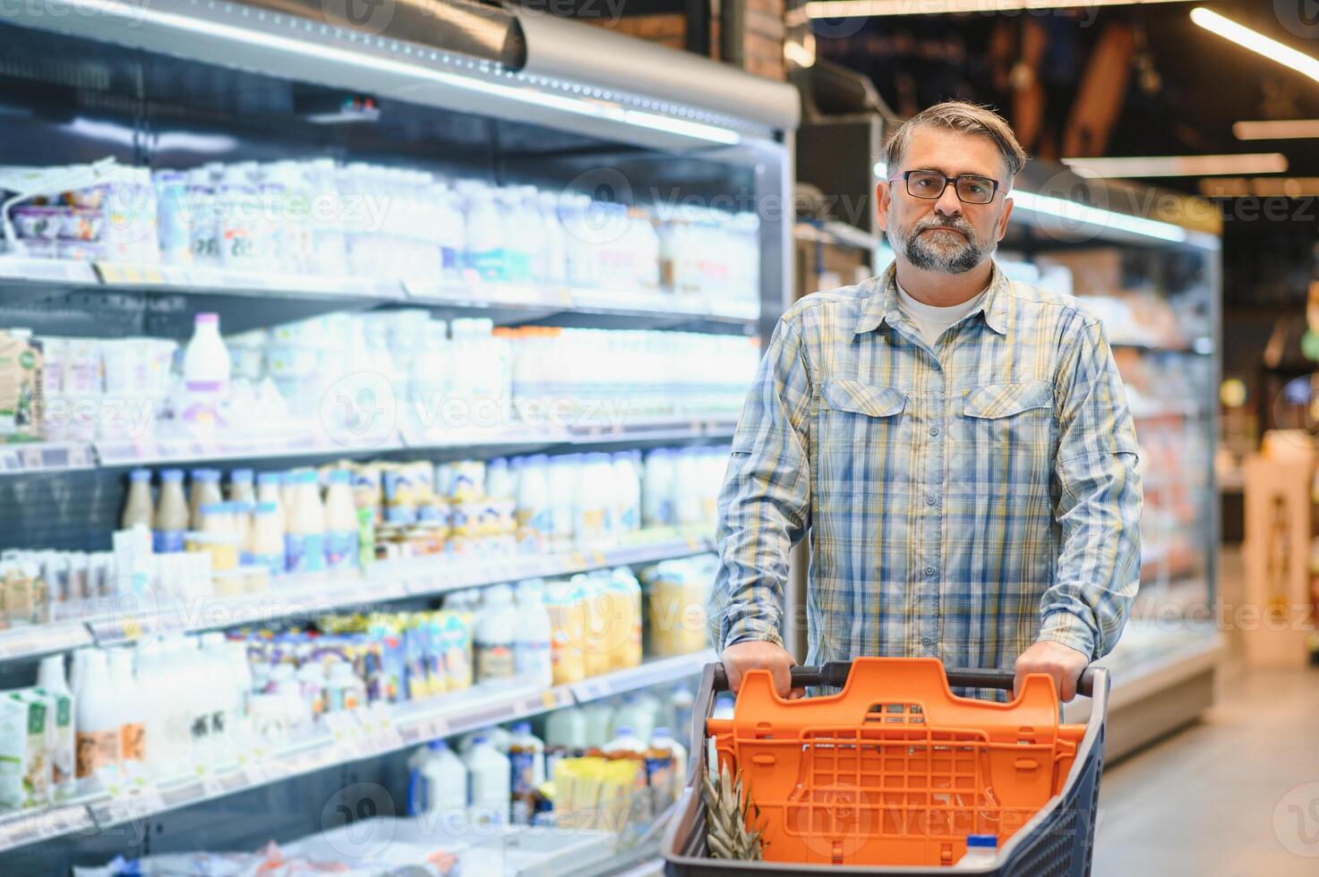 Mature man pushing a shopping cart at the supermarket, he is buying groceries, grocery shopping concept photo