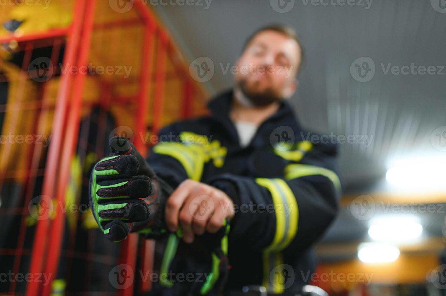Fireman putting on protective uniform and preparing for action while standing in fire station photo