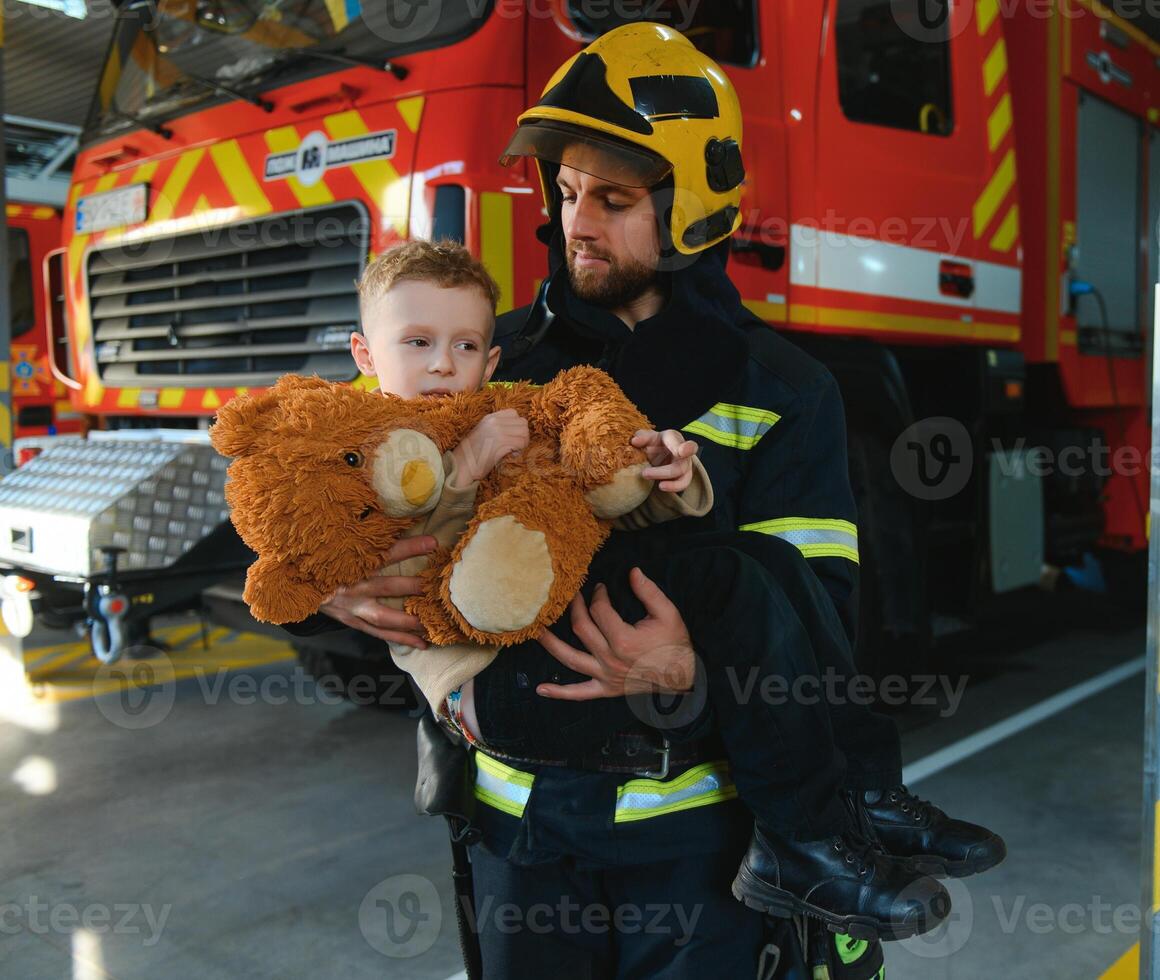 A firefighter take a little child boy to save him. Fire engine car on background photo