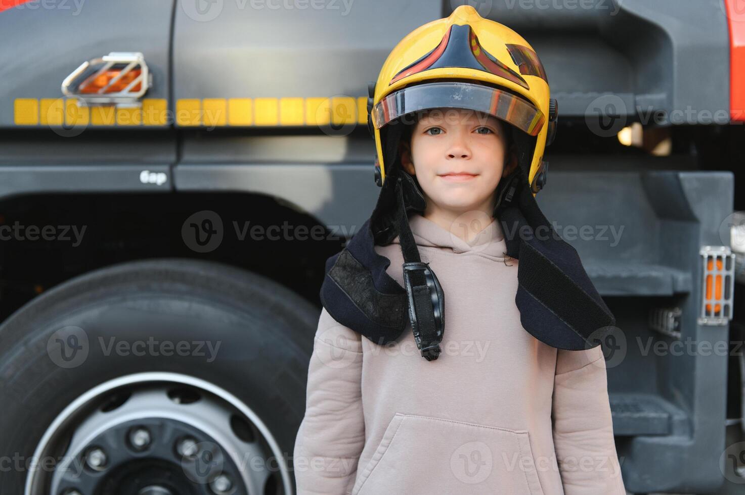 A boy wearing a fireman's helmet near a fire truck. photo