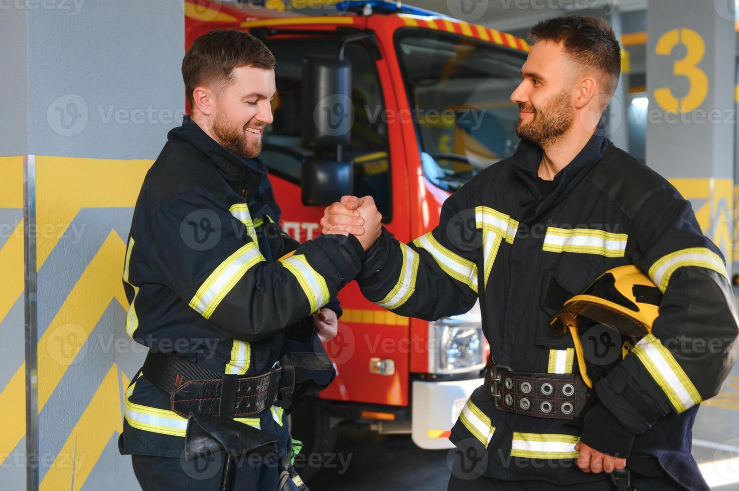 Portrait of two young firemen in uniform standing inside the fire station photo