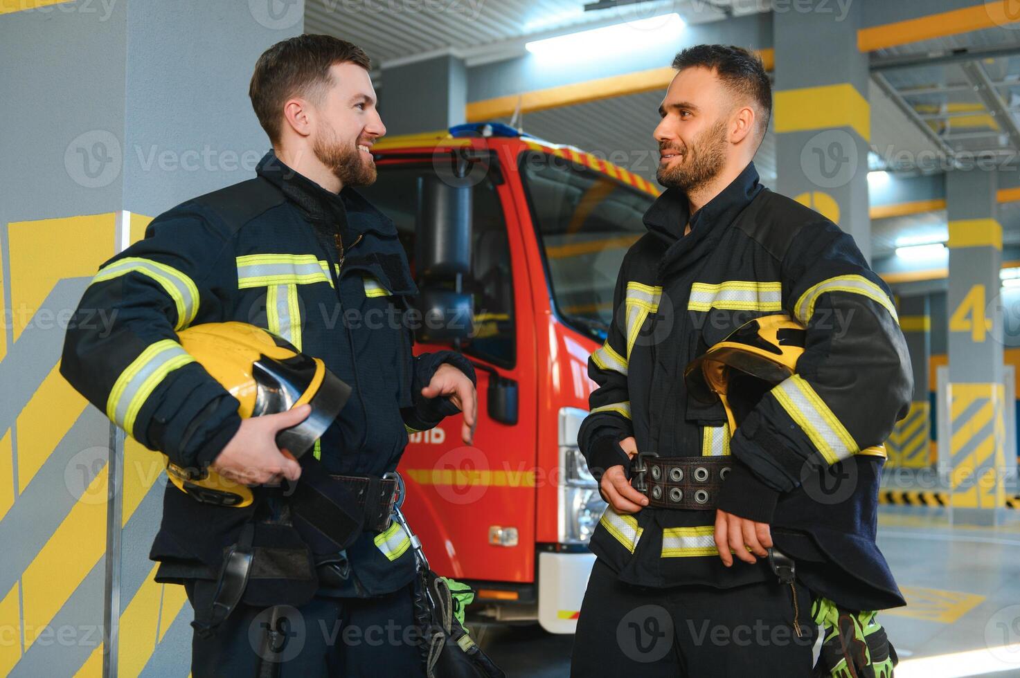 Portrait of two young firemen in uniform standing inside the fire station photo