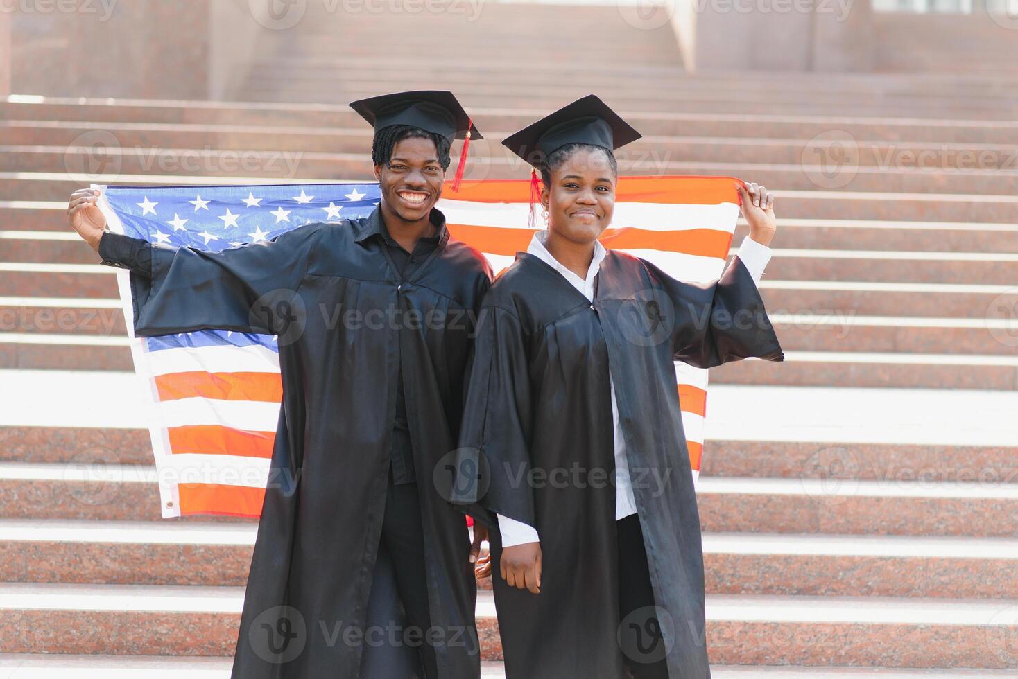 education, graduation and people concept - happy international students in mortar boards and bachelor gowns with american flag photo