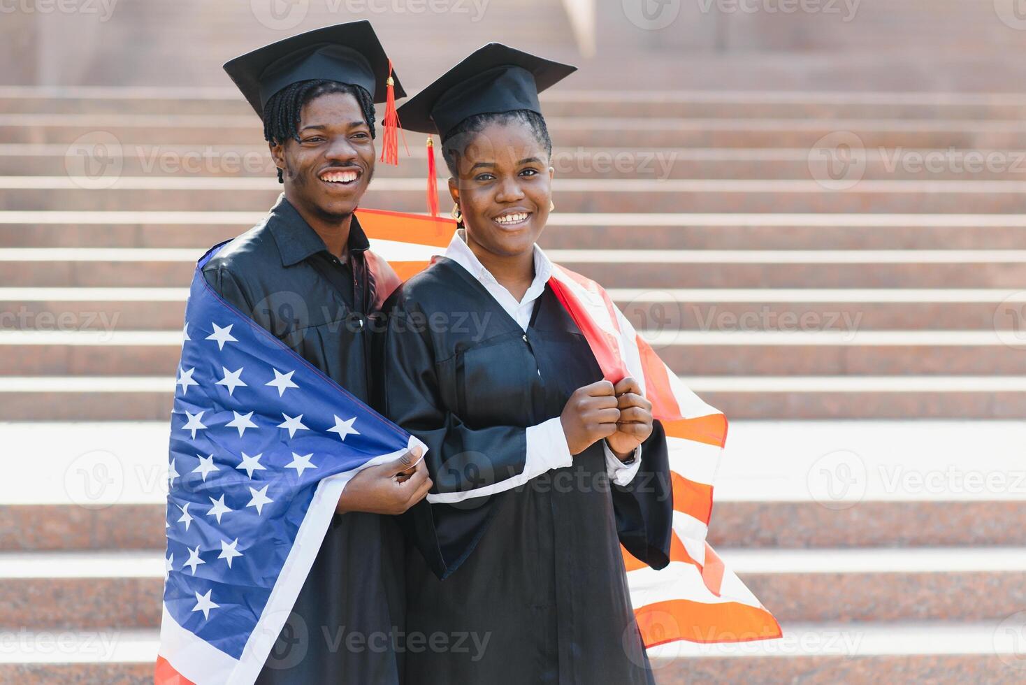 education, graduation and people concept - happy international students in mortar boards and bachelor gowns with american flag photo