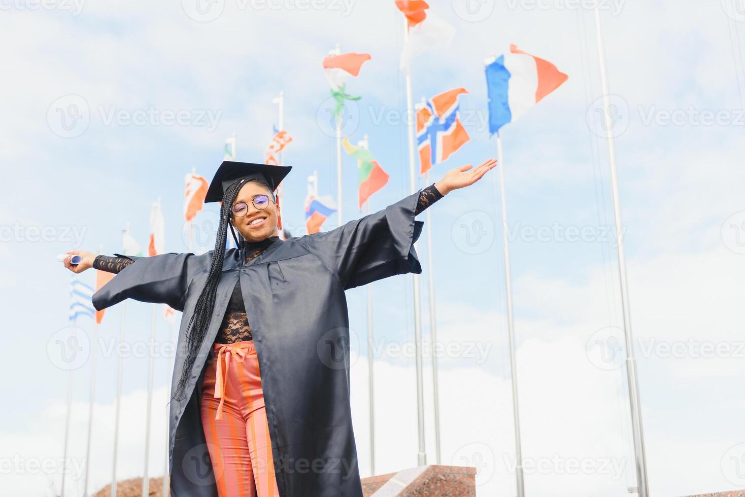 pretty african college student in graduation cap and gown in front of school building photo