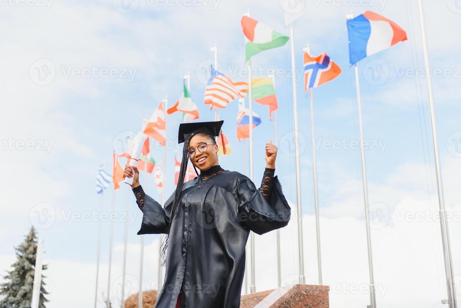 pretty african college student in graduation cap and gown in front of school building photo