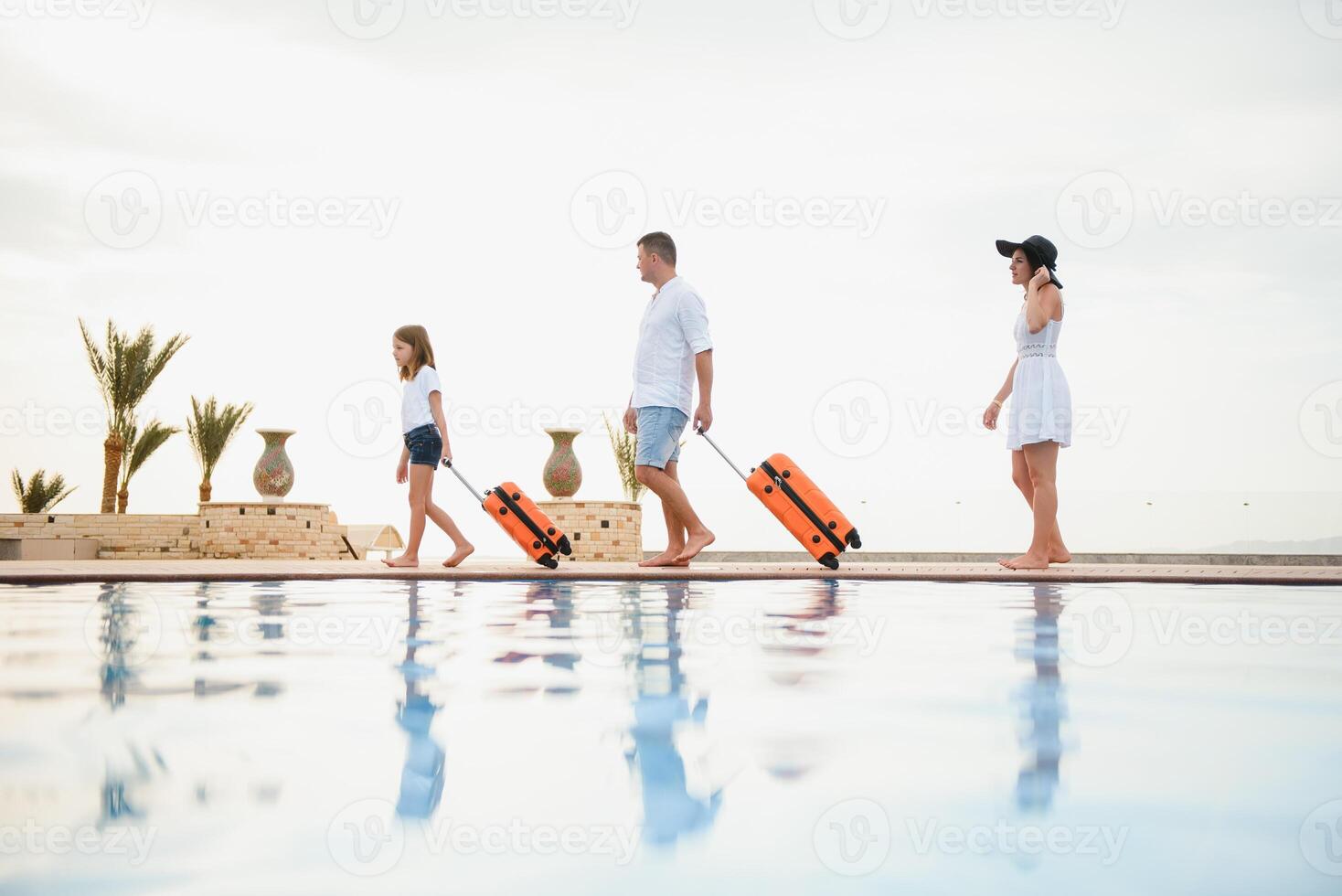 young family with suitcases walking to hotel building with beautiful swimming pool. traveling and relaxing time concept. photo