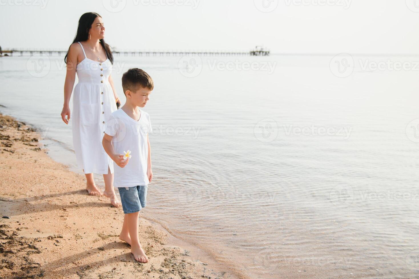 mother and son walking on sunset beach photo