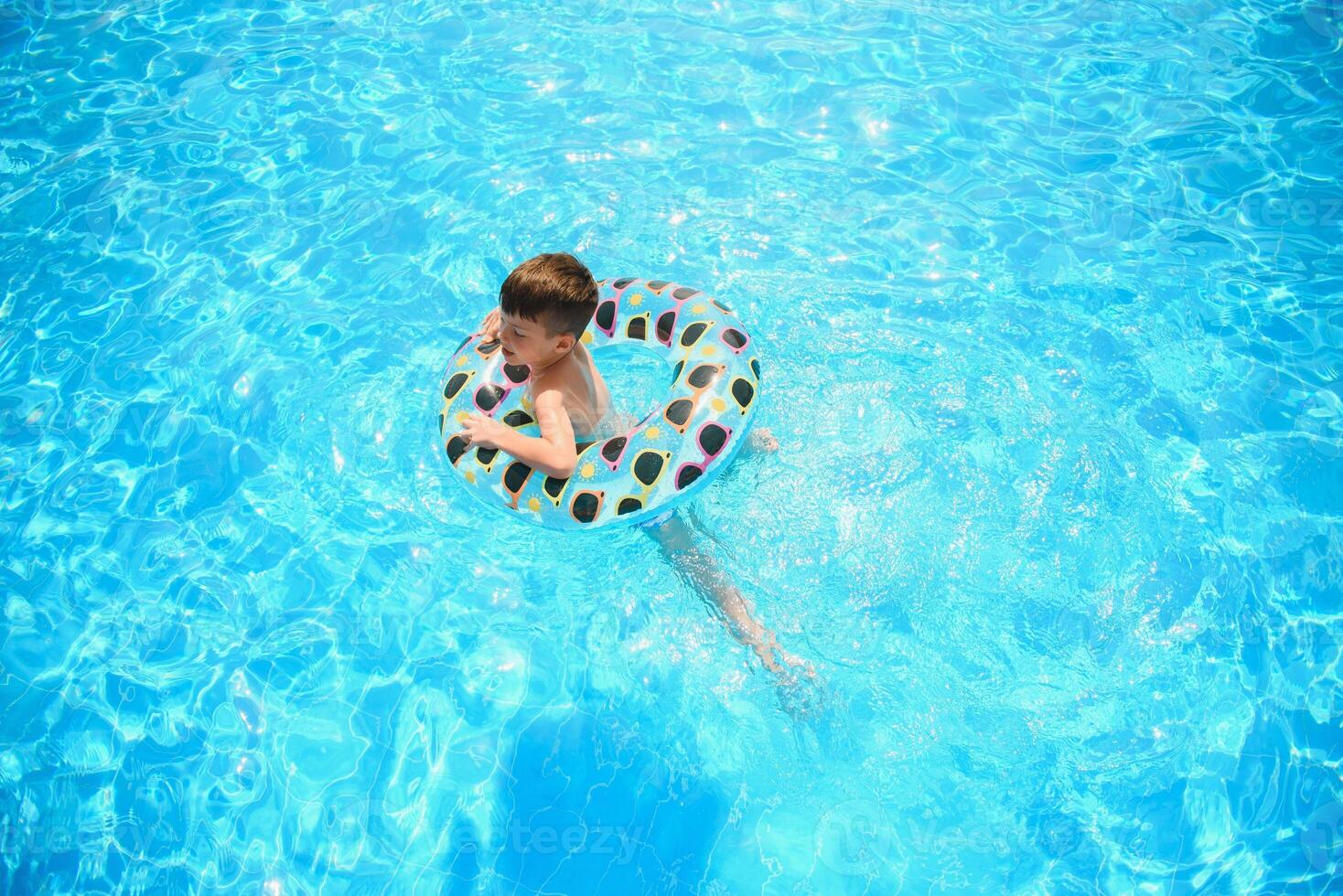 Kids summer vacation. Child swimming in pool. Kids having fun at aquapark. Funny boy on inflatable rubber circle. Summertime. Attractions concept photo