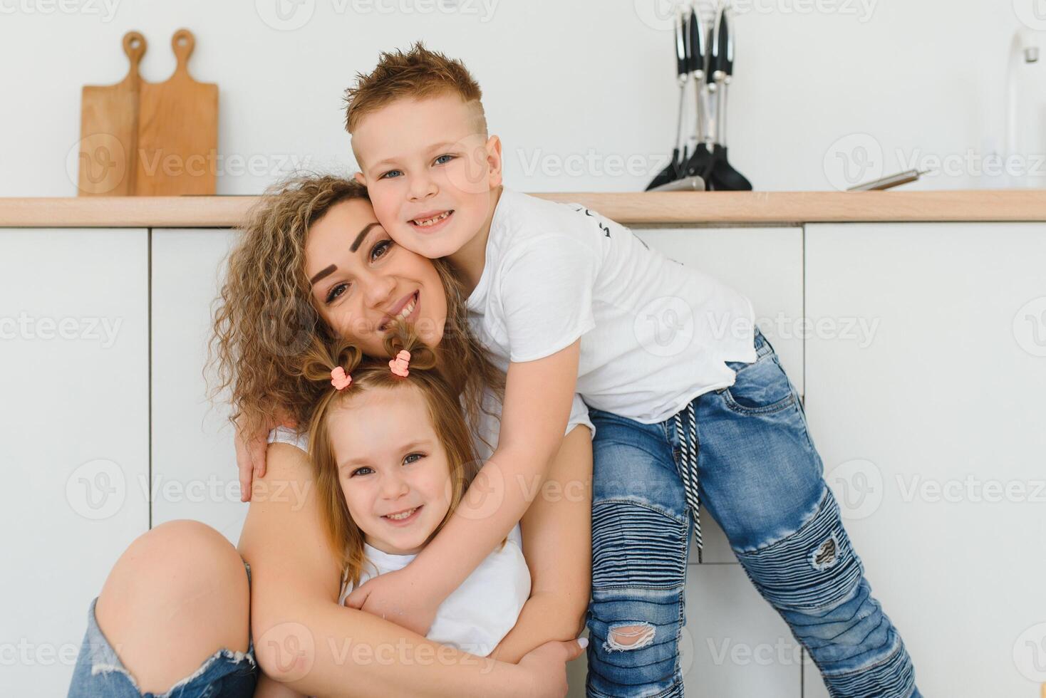 Happy young family, mom with little children sit on warm wooden floor in new modern design kitchen, mother with excited small kids relax rest in own renovated apartment, moving concept photo