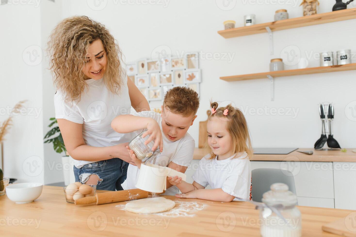 familia aprendizaje nuevo receta juntos. contento mamá y niños mezcla ingredientes para hecho en casa pastel, tarta o Galleta masa en el cocina. foto