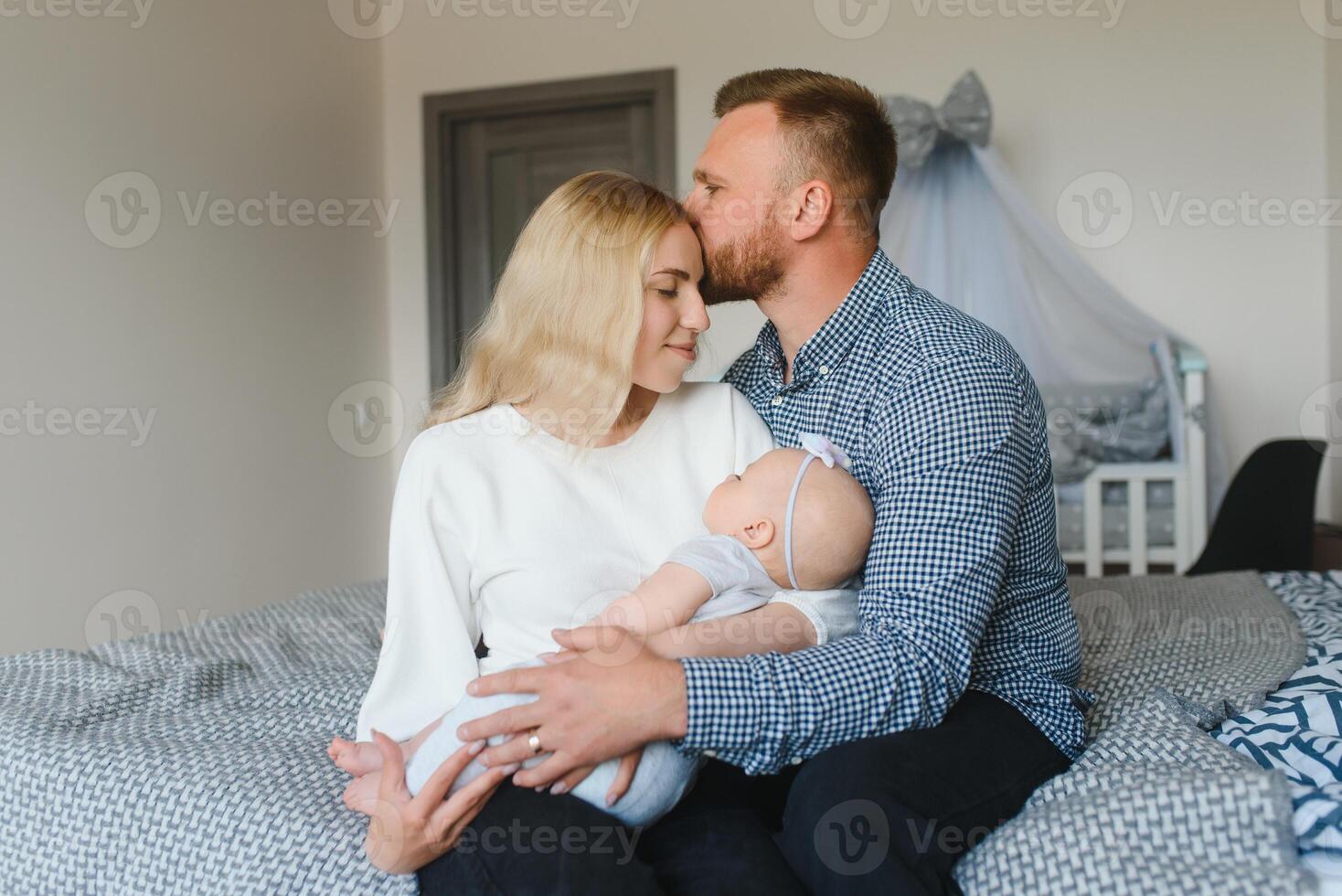 Portrait of happy young parents with baby in the bed at home photo