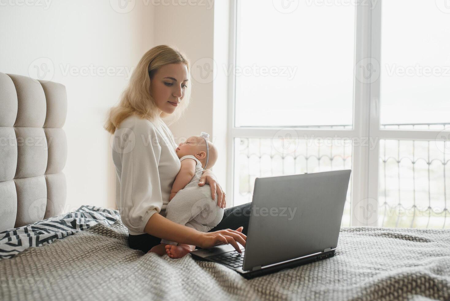 young woman with a small child works from home. Working remotely during a lockdown. freelancer or remotely employed specialist is sitting on a bed with a laptop and trying to concentrate photo
