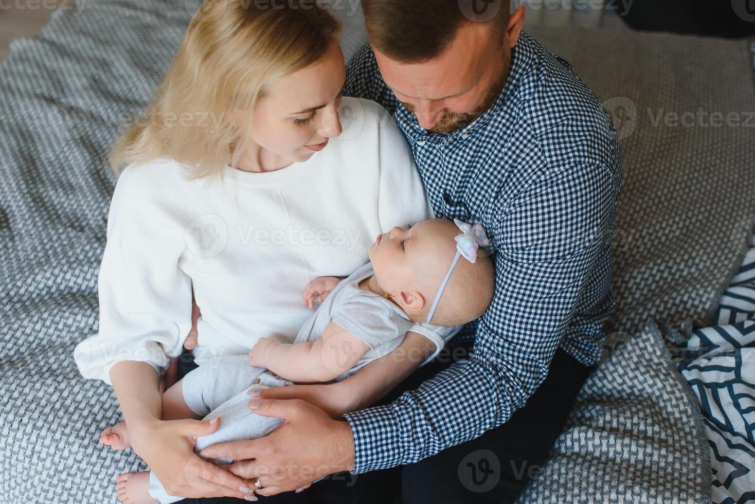 Portrait of happy young parents with baby in the bed at home photo