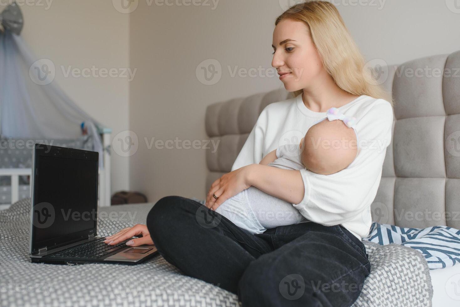 young woman with a small child works from home. Working remotely during a lockdown. freelancer or remotely employed specialist is sitting on a bed with a laptop and trying to concentrate photo