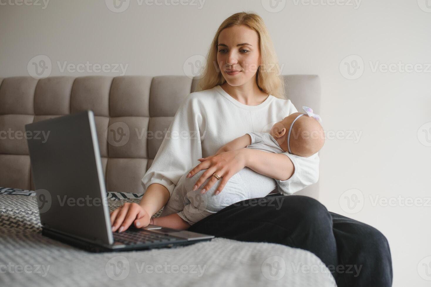 young woman with a small child works from home. Working remotely during a lockdown. freelancer or remotely employed specialist is sitting on a bed with a laptop and trying to concentrate photo