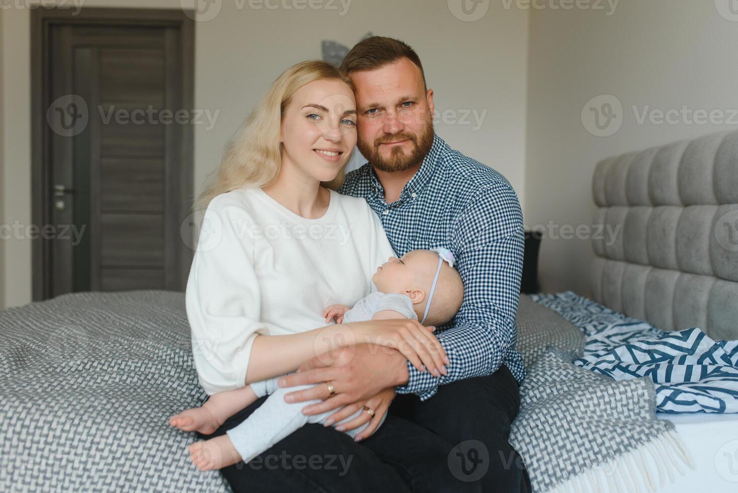 Portrait of happy young parents with baby in the bed at home photo