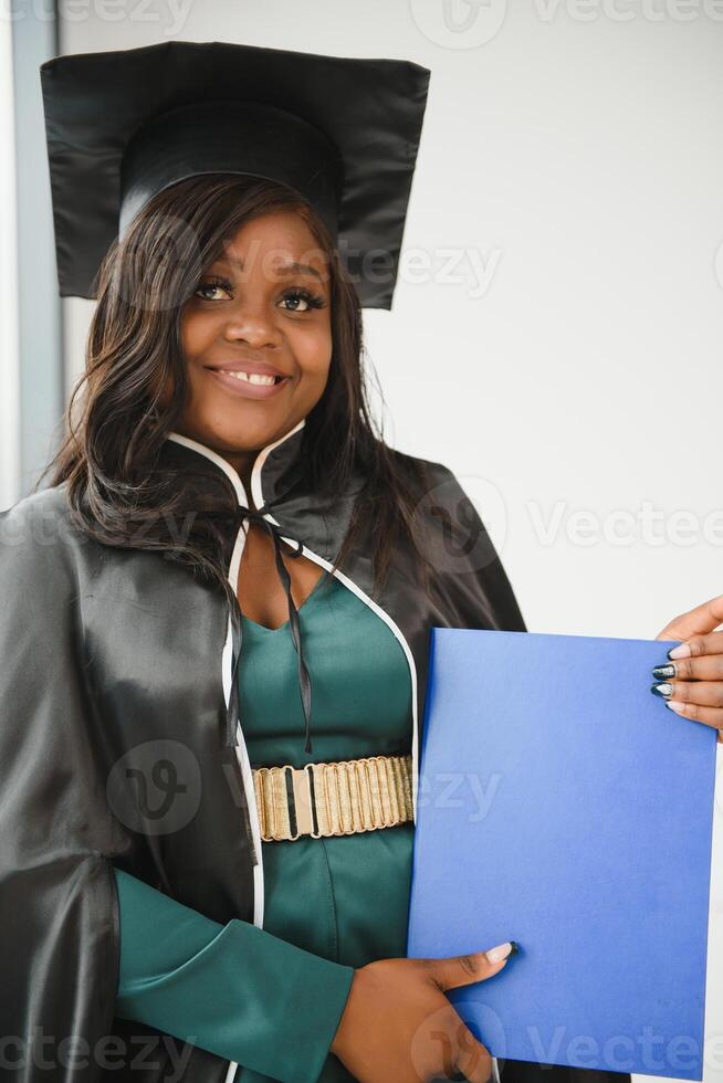 Happy Indian university student in graduation gown and cap holding diploma certificate. Portrait of mixed race Asian Indian and African. photo