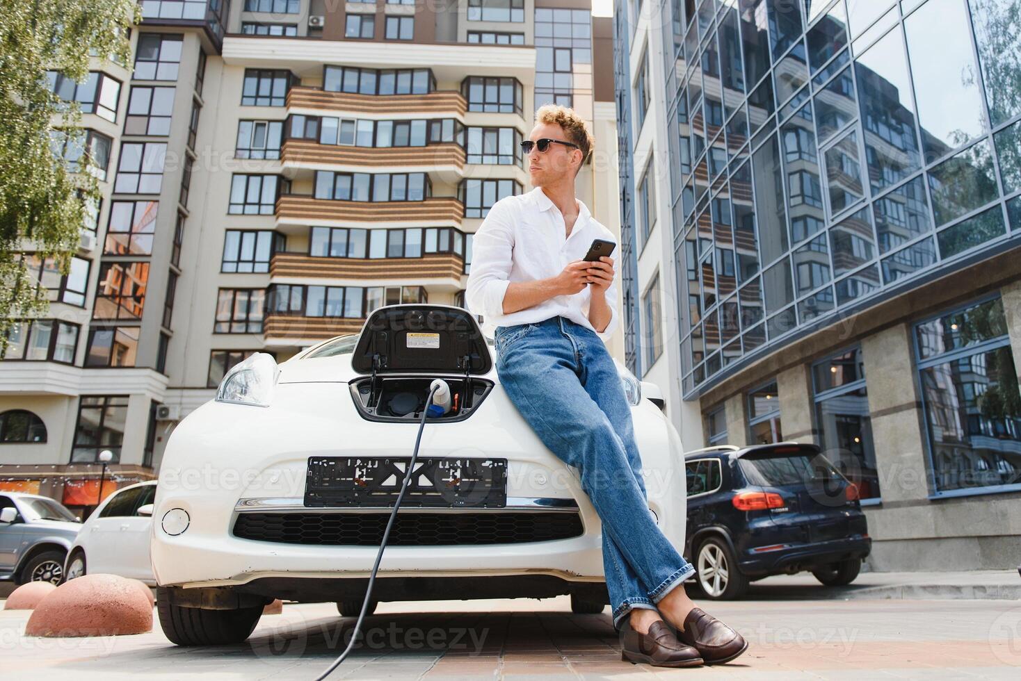 Man with smartphone after finishing charging of battery. Male near electric vehicle photo