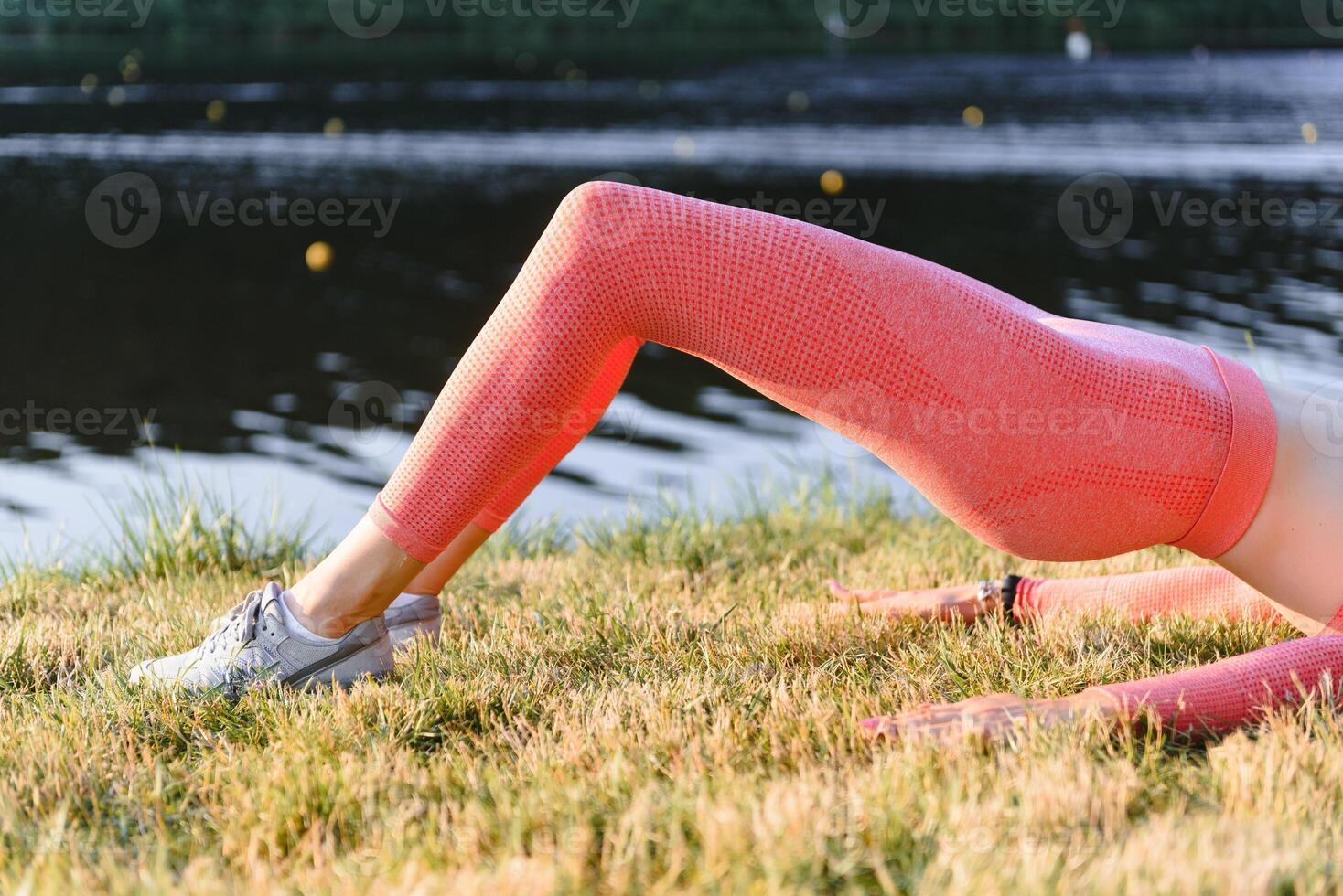 Young caucasian woman doing active training exercise on a yoga mat near the river in summer. Concept of healthy lifestyle photo