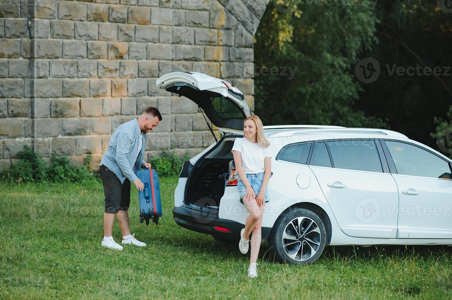 Young couple standing near the opened car boot with suitcases. photo