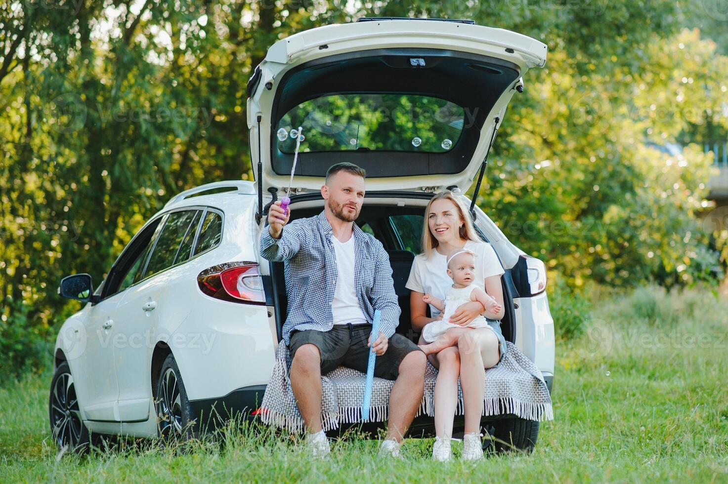Young family three people in white clothes have picnic. Beautiful parents and daughter travel by car during summer vacation. Scene in park photo