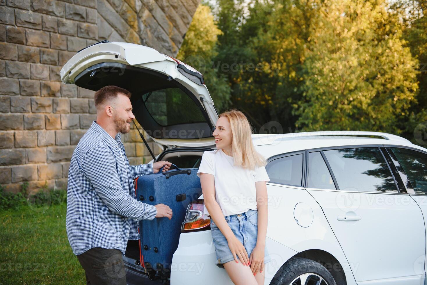 Young couple standing near the opened car boot with suitcases. photo