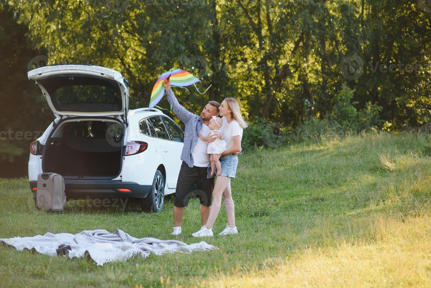 Young family three people in white clothes have picnic. Beautiful parents and daughter travel by car during summer vacation. Scene in park photo