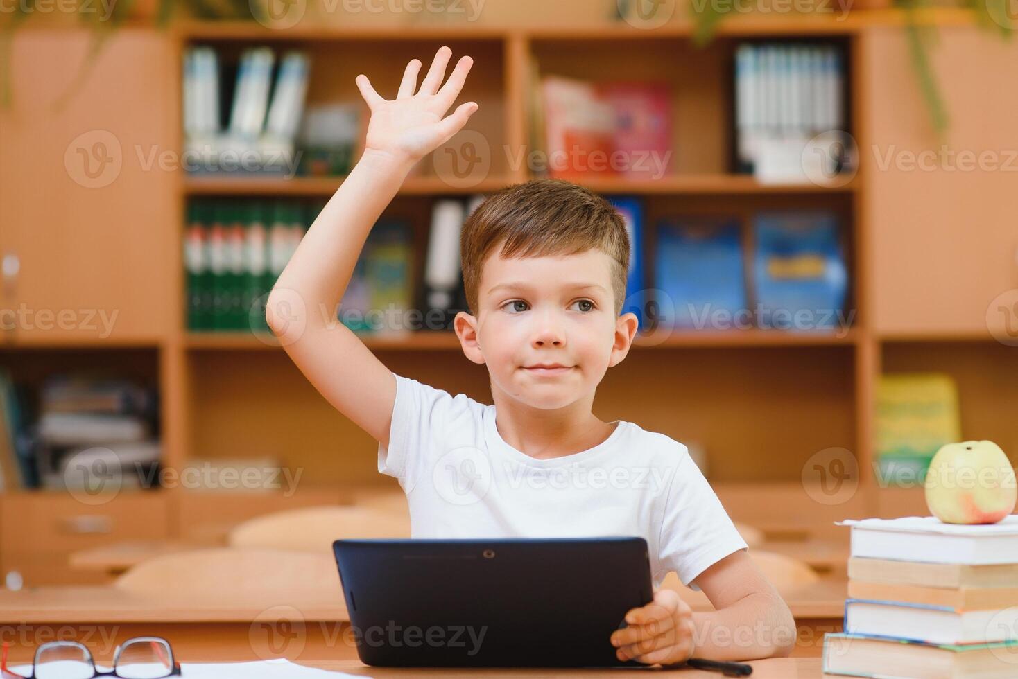 Elementary schoolboy using digital tablet with classmate studying in background at classroom photo