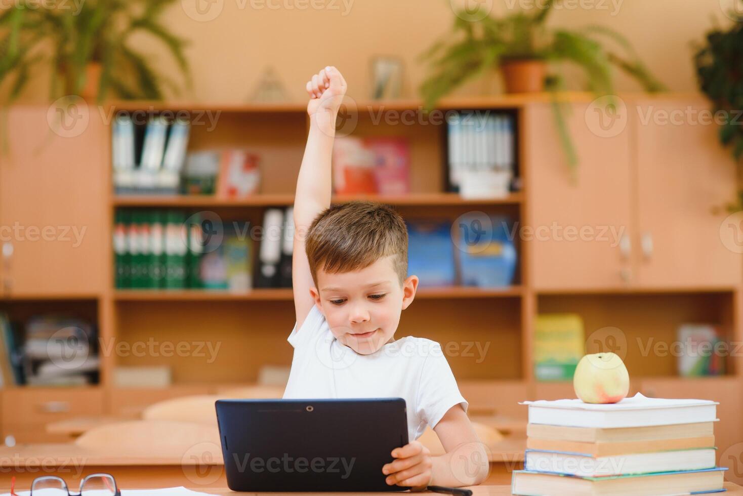 Elementary schoolboy using digital tablet with classmate studying in background at classroom photo