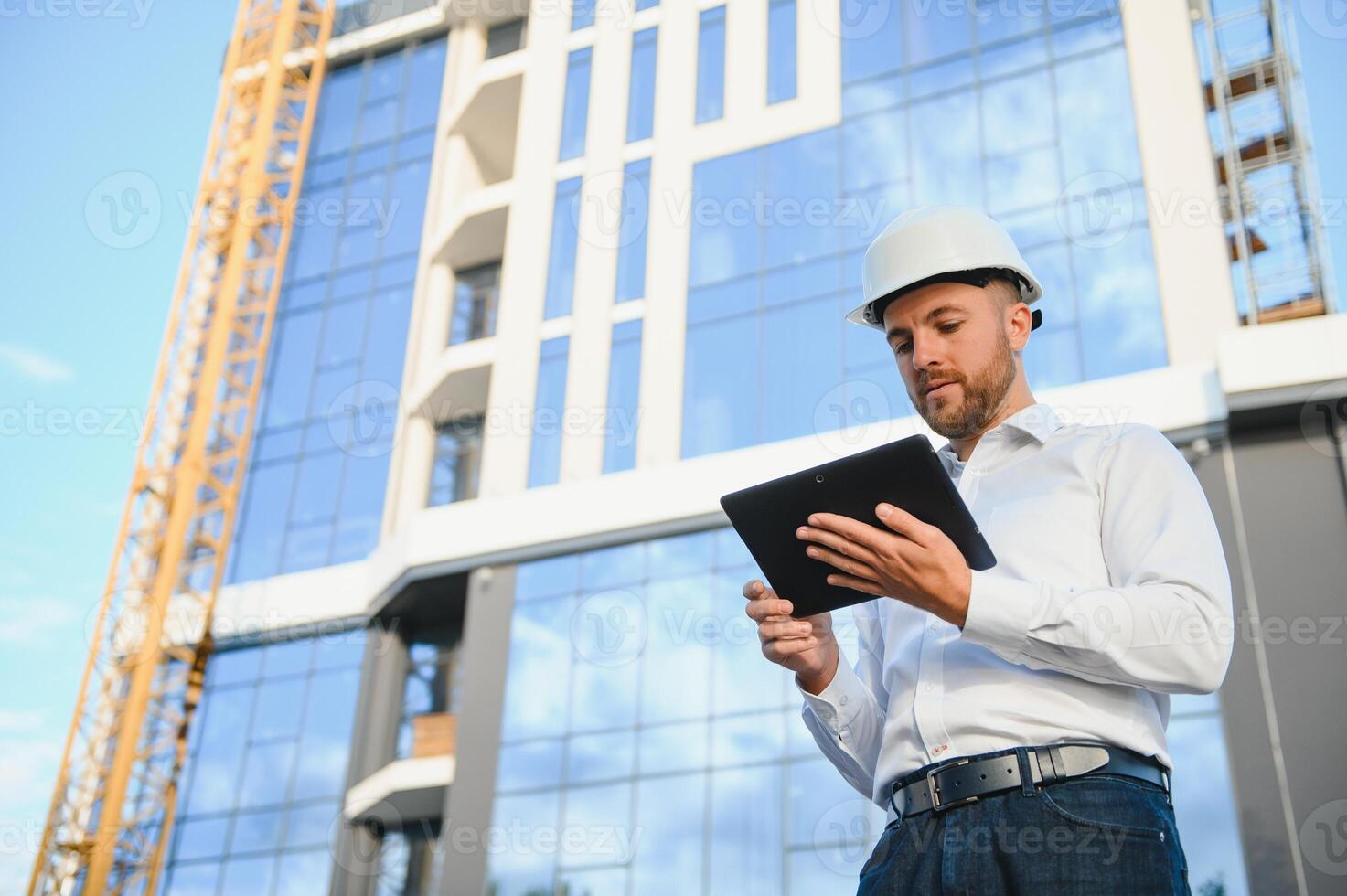 Engineer next to building cranes. Concept - large construction project. Architect directs the construction process. Drawings and tablet in the hands. photo