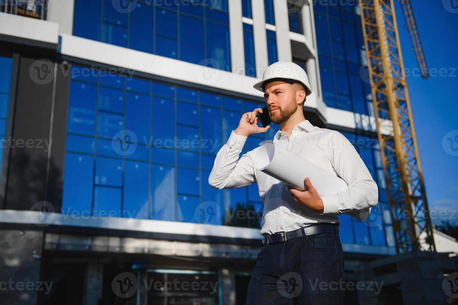 Successful engineer or architect, crane and building construction at backgrpound. Joyous businessman with wearing helmet. photo