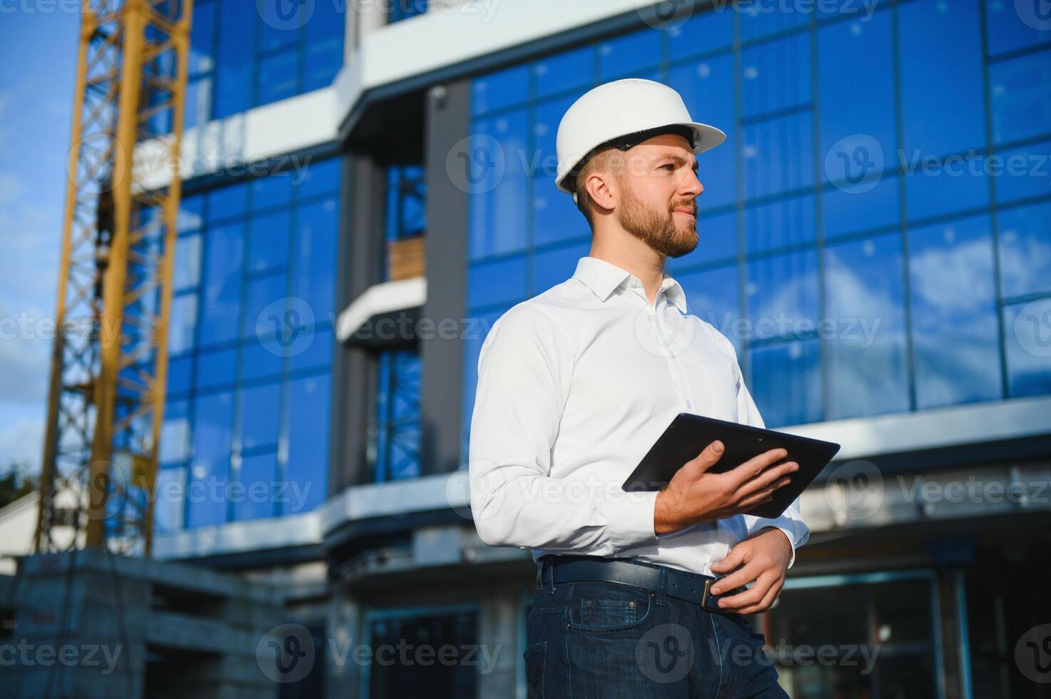 Engineer next to building cranes. Concept - large construction project. Architect directs the construction process. Drawings and tablet in the hands. photo