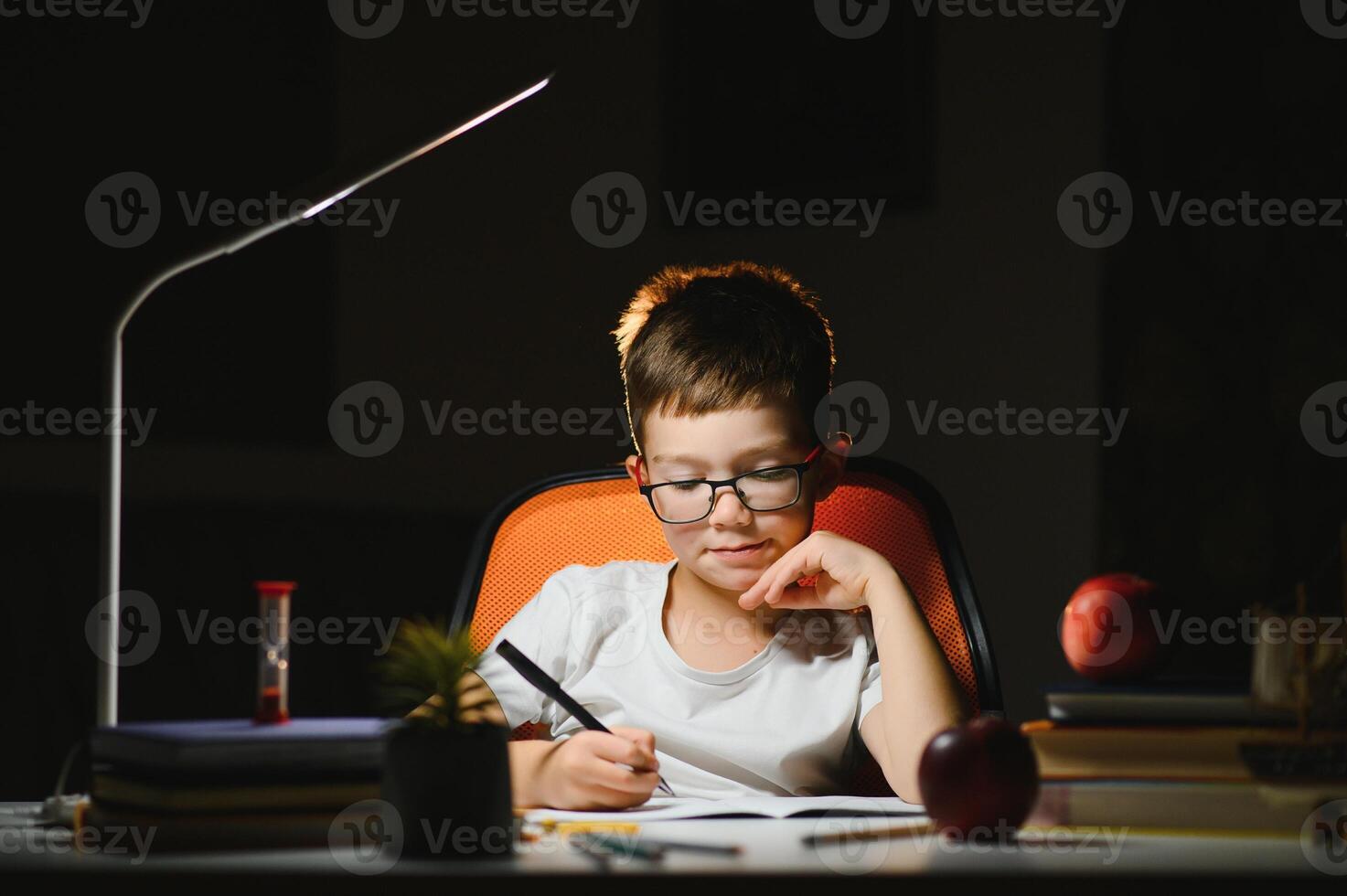 young teenager schoolboy at the table doing homework in the dark room photo