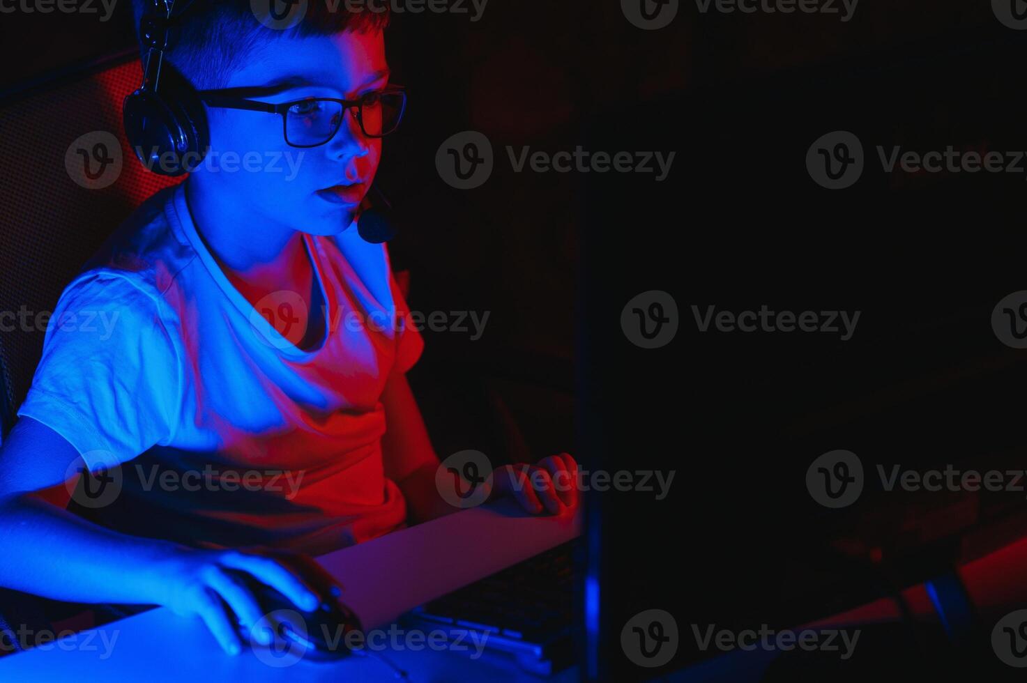 Child online broadcasts computer game, boy streams in headphones on rgb lighting background photo