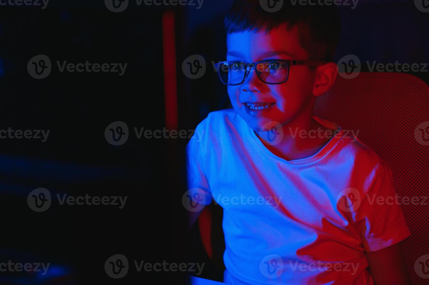 Child online broadcasts computer game, boy streams in headphones on rgb lighting background photo