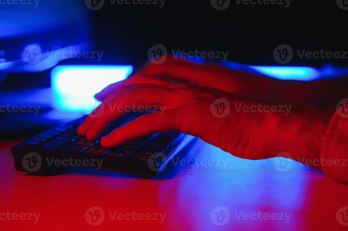 Close-up On Gamer's Hands on a keyboard, Actively Pushing Buttons, Playing MMO Games Online. Background is Lit with Neon Lights. photo
