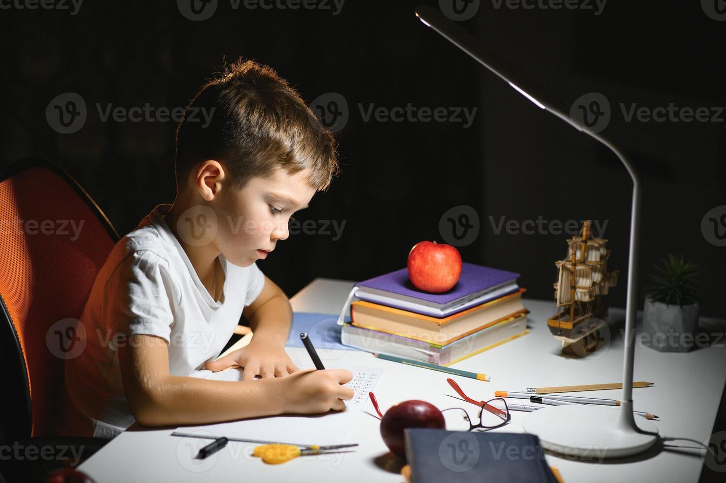 young teenager schoolboy at the table doing homework in the dark room photo