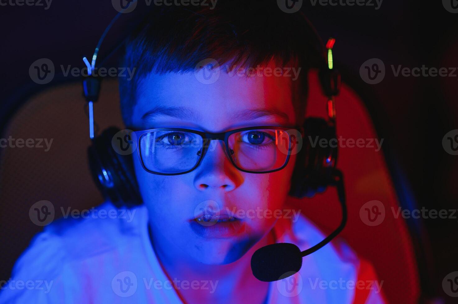 Child online broadcasts computer game, boy streams in headphones on rgb lighting background photo