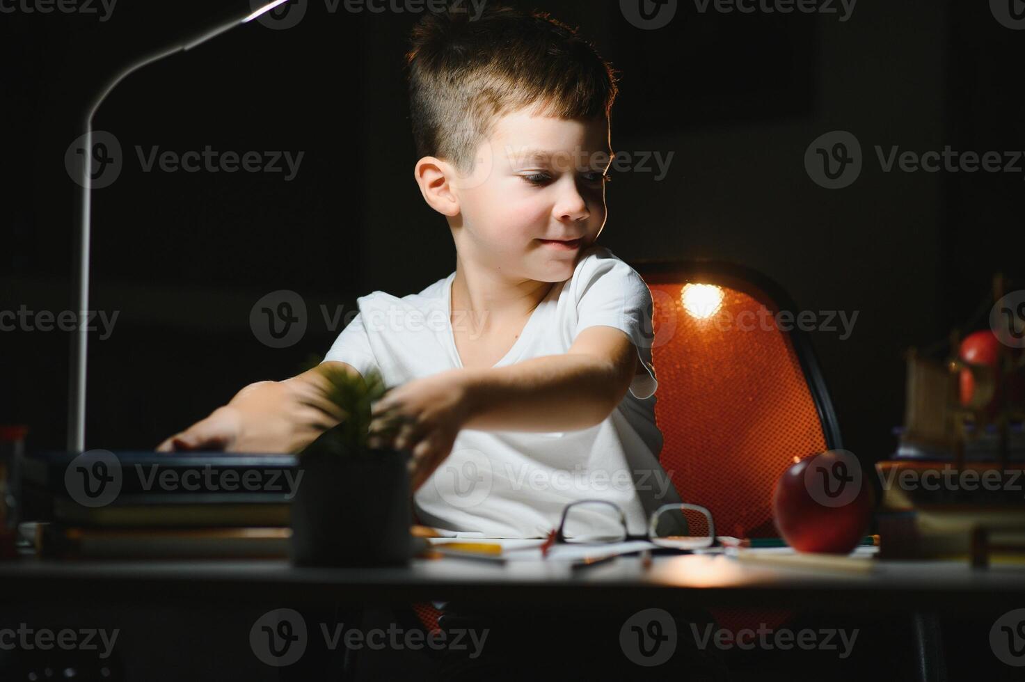 Happy child reading book at table with lamp. photo