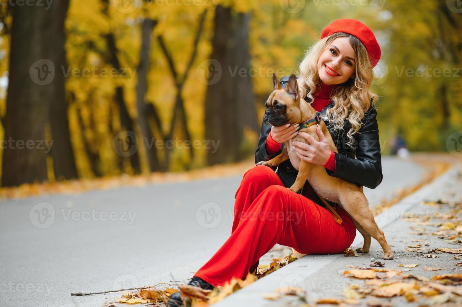 a stylish young girl with long light hair in sunny glasses goes for a walk with a little middle doggy a pug by the French bulldog in a park in spring in autumn photo