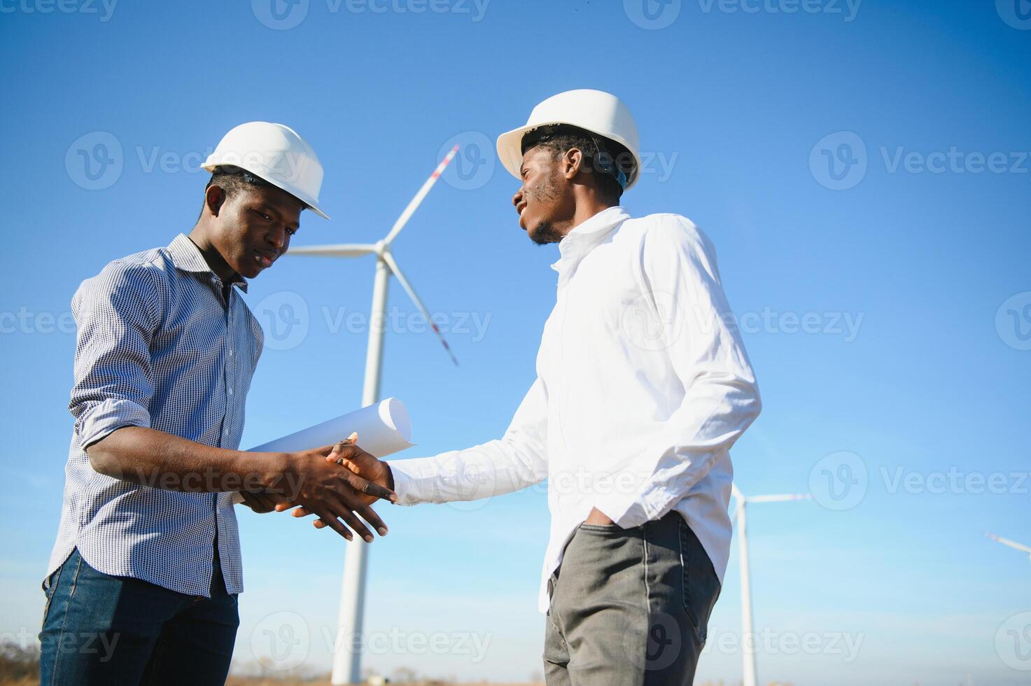 Young maintenance engineer team working in wind turbine farm at sunset stock photo
