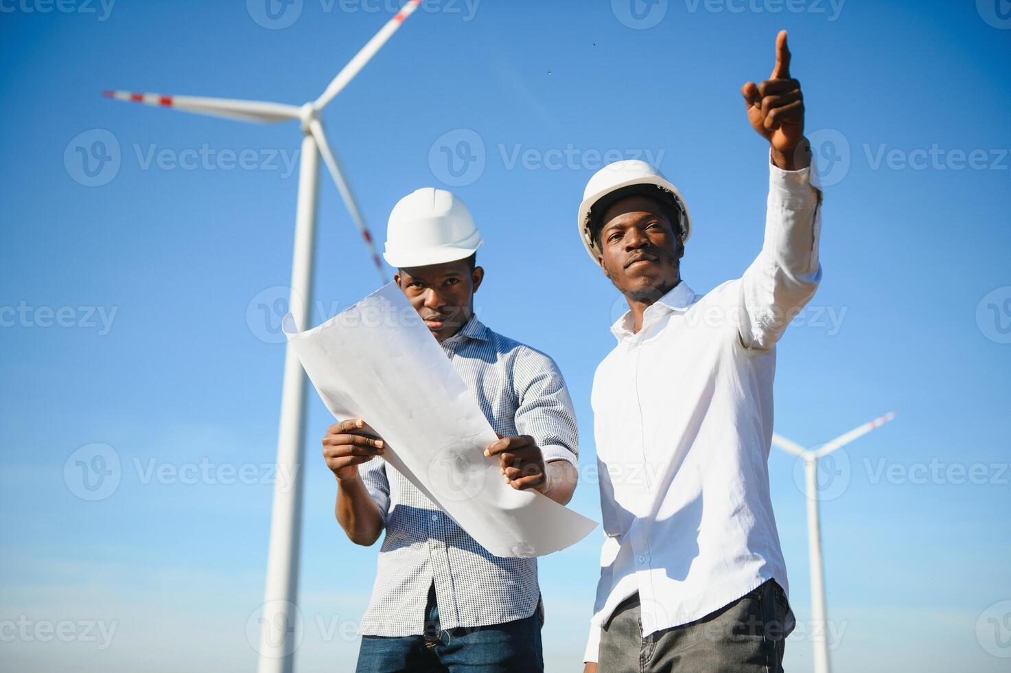 Young maintenance engineer team working in wind turbine farm at sunset stock photo