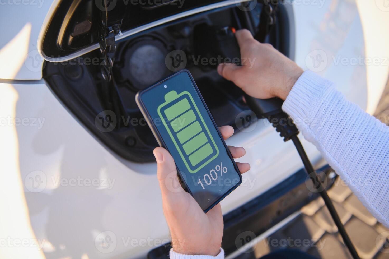 Man Charging Electric Vehicle With Cable Looking At App On Mobile Phone photo