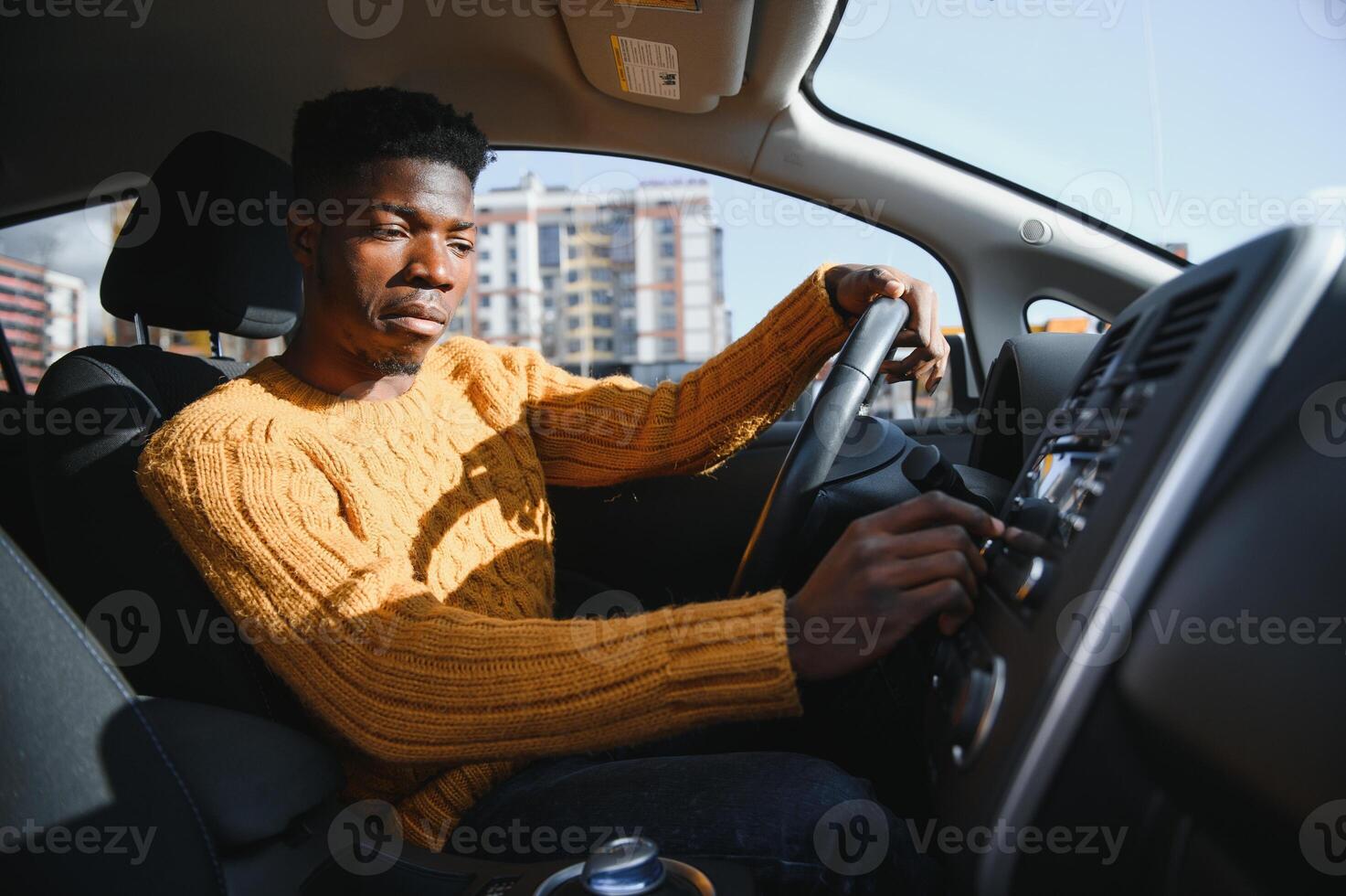 Smiling African American young man, sitting in the cabin of a comfortable modern electric car and touching the screen of navigation self-driving autopilot photo