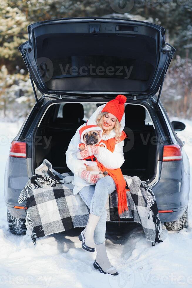 Woman resting in the winter forest sitting in the open trunk of a car with a dog. photo