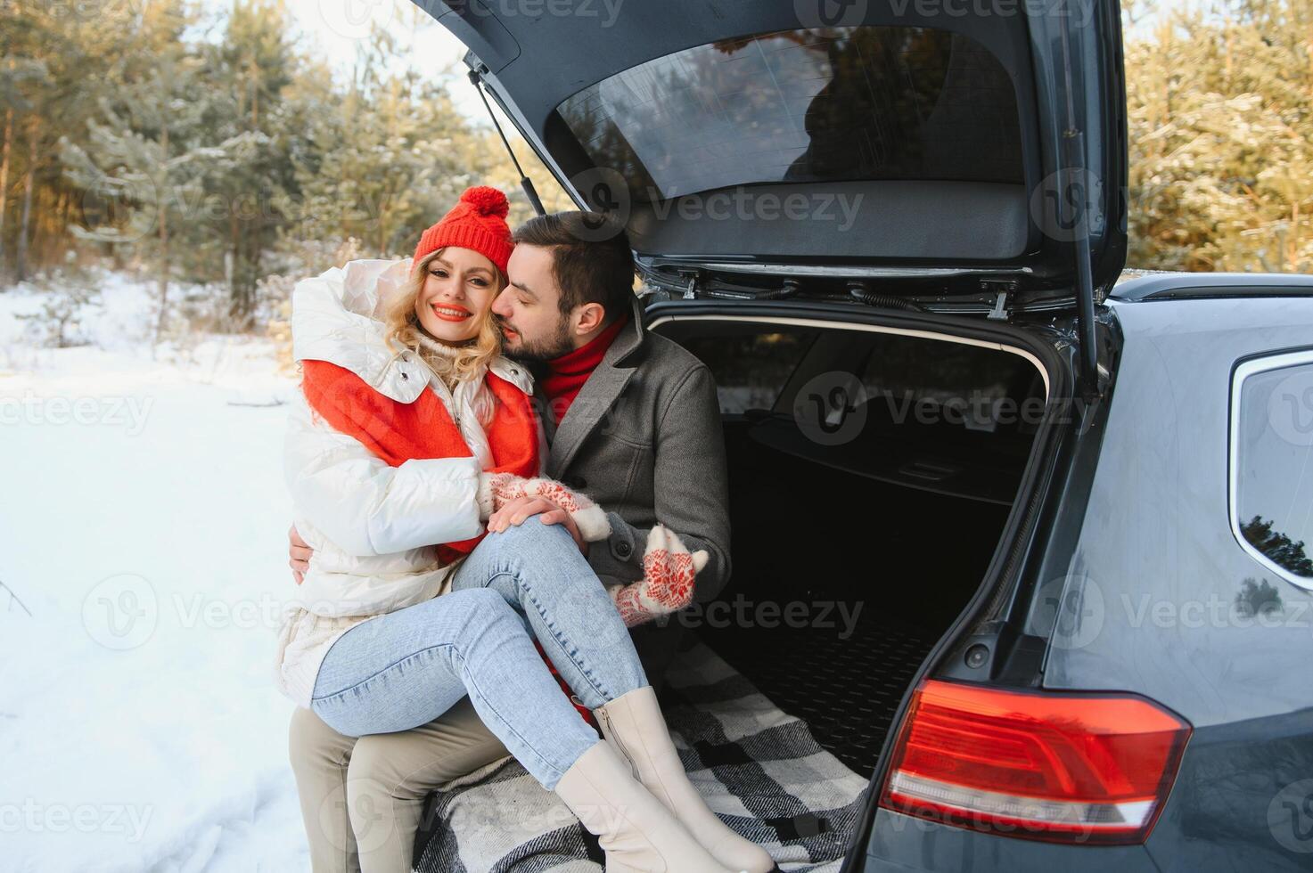 Smiling together. Nice couple have weekend at countryside at winter time. Sitting on the rear part of modern car. photo